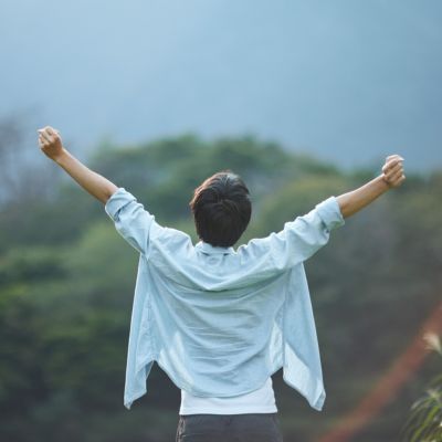 Person mit hochgereckten Armen Person mit hochgereckten Armen in hellblauen Hemd vor grünem Hintergrund (verschwommene Natur).