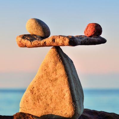 In Balance Steine in Balance - ein flacher Stein liegt auf der Spitze von einem Stein, der wie eine Pyramide geformt ist. Auf dem flachen Stein liegen rechts und links kleinere, runde Steine