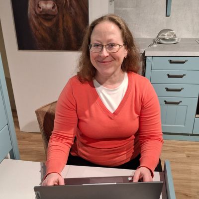 Melanie am Laptop Laptop auf Holztisch und Frau schaut lächelnd auf das Display vom Laptop, welches man nicht sehen kann. Ansicht leicht von oben