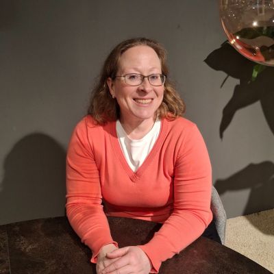 Frau am Tisch lächelt in die Kamera.