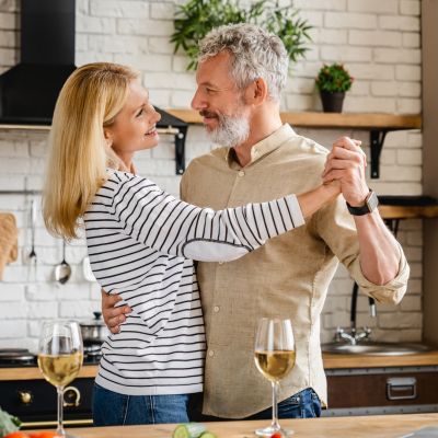 Tanzendes Paar Frau sitzt am Laptop in der Küche und schaut über den Laptop lächelnd in die Kamera