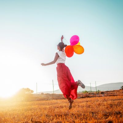 Frau mit bunten Luftballons hüpft in die Luft
